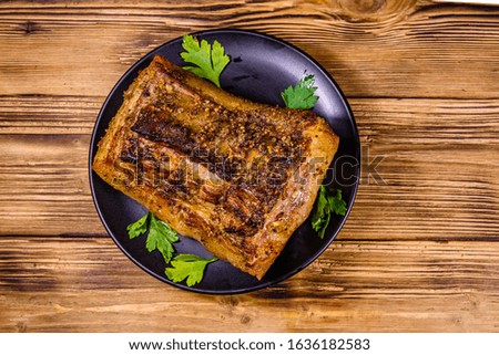 Baked piece of pork belly and parsley on black plate