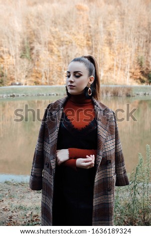  Close up portrait of Fashion pretty brunette woman wearing coat in the cage standing near the lake. Trendy modern female fashion concept.