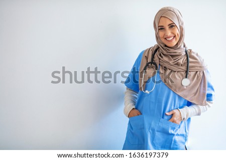 Cheerful young Muslim female nurse portrait, standing inside hospital. Arab female doctor posing and smiling isolated on a white background. Arab nurse woman wearing hijab over isolated background