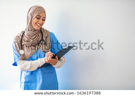 A female Malaysian medical doctor stands proudly and smiles as she carries a medical record under her arm. Closeup portrait of friendly, smiling confident muslim female doctor