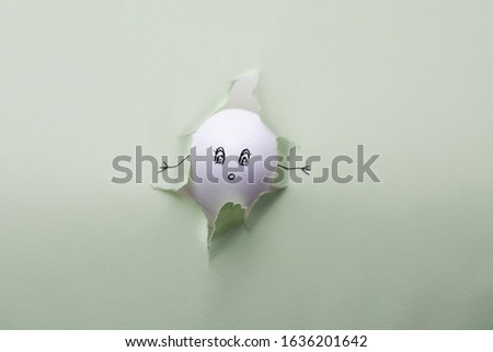 Funny egg with drawn face trying to climb out of the cardboard. Creative image, easter concept