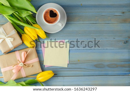 Morning coffee with tulips flowers and gifts on blue wooden background. Spring concept. 