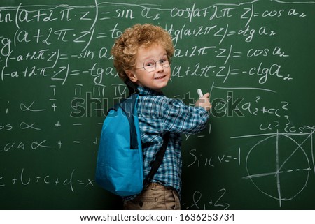 happy kid in glasses writing mathematical formulas on chalkboard