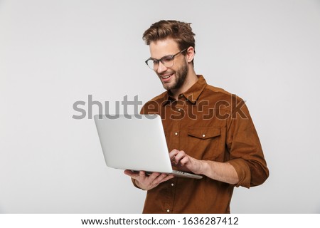 Portrait of cheerful young man wearing eyeglasses using laptop and smiling isolated over white background Royalty-Free Stock Photo #1636287412