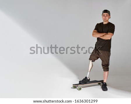 Disabled young man with leg prosthesis with longboard skateboard on white background. Sun light.
