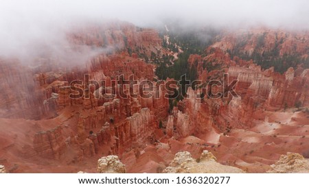 The photo shows a landscape in Bryce Canyon National Park, Utah. The picture offers a view from the break-off edge into the Paria valley. Wafts of mist drift over the reddish erosional rock.