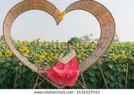 woman in Korean dress sitting in bamboo hearth shaped over  sunflower Garden.