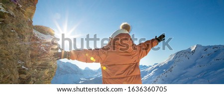 A picture of a beautiful woman looking at a mountain with a lot of snow happily as a holiday vacation and enjoying nature in the mountains. The famous GRINDELWALD-FIRST of Switzerland.