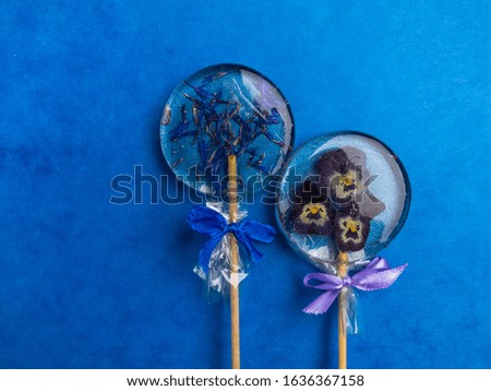 Lollipop, Blue Cornflower Herb, pansies, decorated with bows, on trendy blue classic background, flat lay minimal concept. Herbal medicine, flowers used in natural herbal medicine and homeopathic