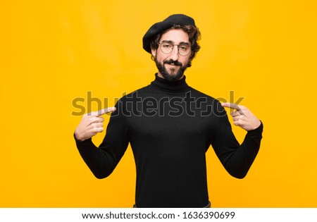 young french artist man looking proud, positive and casual pointing to chest with both hands against orange wall