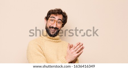 young cool man feeling happy and successful, smiling and clapping hands, saying congratulations with an applause against flat wall