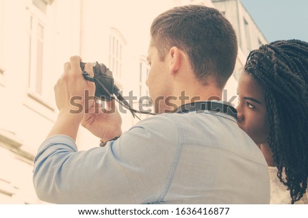 Interracial couple travelling together. Young Caucasian man and Afro American woman taking pictures in old city alley. Travel and photography concept