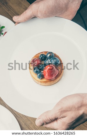 Waiter bringing fruit dessert. Above view of unrecognizable man holding plate with delicious cake decorated with berries. Restaurant menu concept