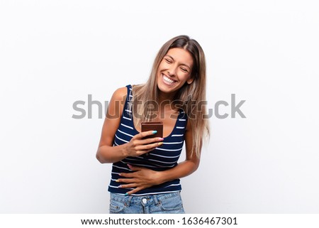 young pretty woman laughing out loud at some hilarious joke, feeling happy and cheerful, having fun with a leather wallet.