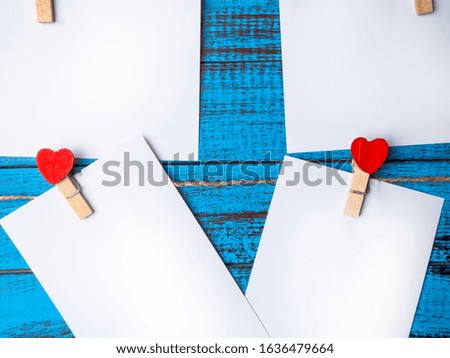 white blank paper sheets on a clothes line and clothespegs with red heart on trendy blue color surface, Valentines day and love concept. Copy space.