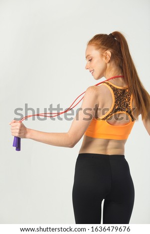 beautiful young slim woman with red hair in sportswear on a white background with a skipping rope in hands