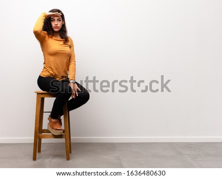 young pretty woman covering face with hand and putting other hand up front to stop camera, refusing photos or pictures sitting into a room