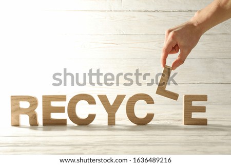 Hand hold L on wooden background with Recycle word, space for text