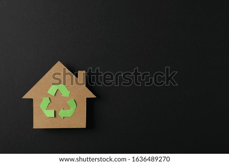 Cardboard house with recycling sign on black background, space for text