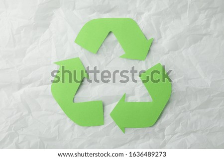Recycling sign on white crumpled paper background, top view