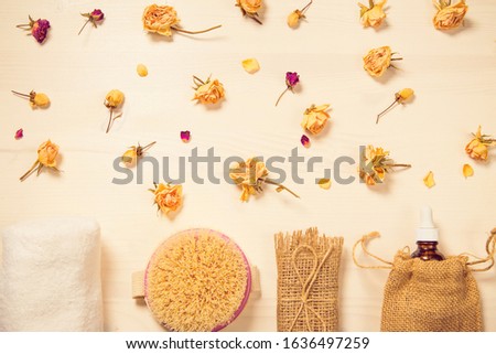 Set of natural soap, aroma oil, white towel and body brush with dried rose buds as a decoration on wooden background. Home spa concept. Beauty rituals theme.
