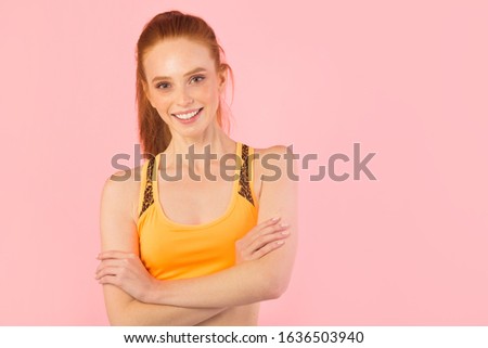 beautiful young slim woman with red hair in sportswear on a pink background