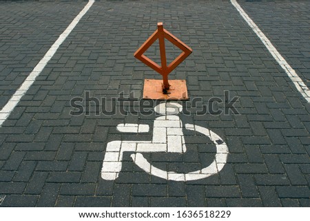 disabled parking sign painted on asphalt with white paint. Folding barrier prevents Parking
