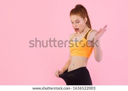 beautiful young slim woman with red hair in sportswear on a pink background