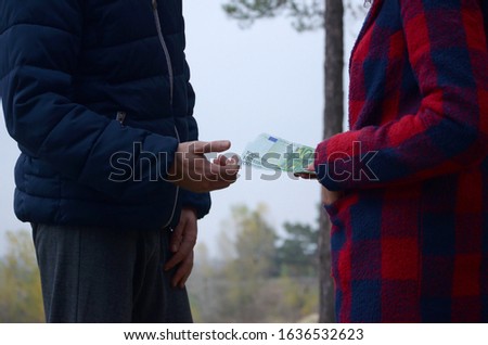 Girl transfers euro bills to the hands of a young guy in forest. Concept of robbery or illegal deal transaction