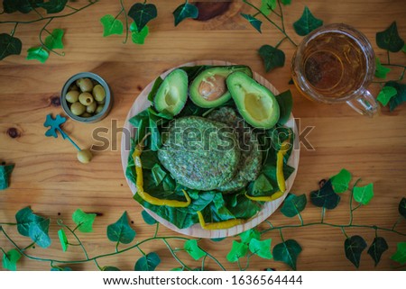 Food to celebrate St. Patrick's Day: healthy and vegetarian spinach burger, avocados, green chillies, olives and beer with a rustic wooden background and leaves