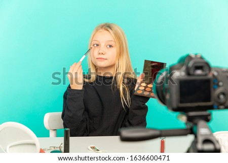 Happy girl in the studio speaking in front of camera for vlog. Young white woman working as blogger, recording video tutorial for Internet.