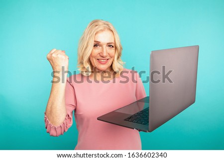 Portrait of happy exited abult lady with laptop isolated over the blue studio.