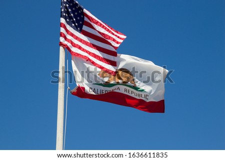 USA and California flags flying in the wind against blue sky.