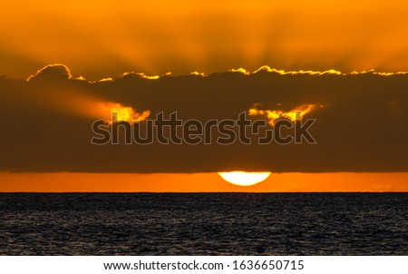 panoramic photo of a glowing Hawaiian sunset over the pacific ocean with sun rays shining through the cloud layer