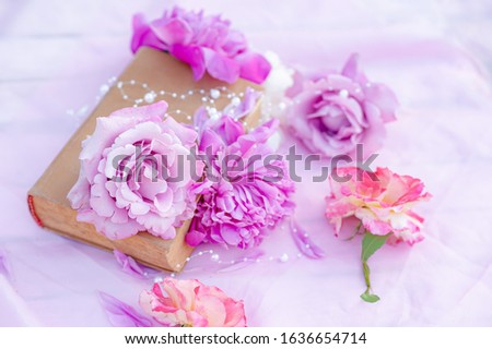 Flat lay of pink peonies on an old book with white beads. Romantic picture