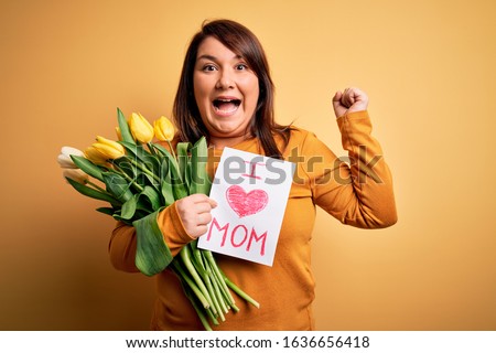 Young beautiful plus size woman celebrating mothers day holding love mom message screaming proud and celebrating victory and success very excited, cheering emotion