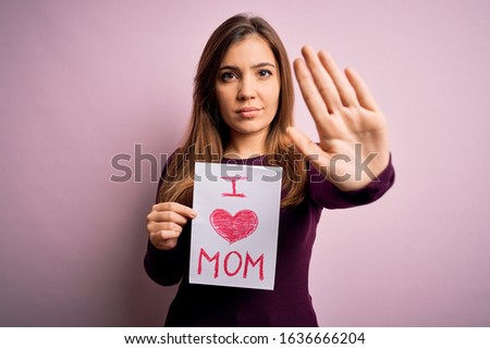 Young beautiful woman holding paper with love mom message celebrating mothers day with open hand doing stop sign with serious and confident expression, defense gesture