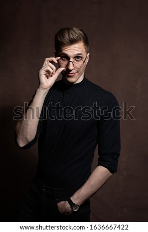 Elegant young man in round glasses, a black shirt on a brown background