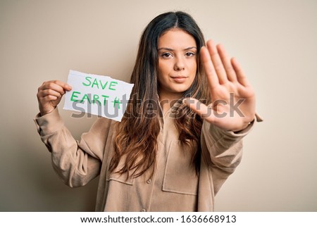 Young beautiful woman holding paper asking for save earth and enviroment conservation with open hand doing stop sign with serious and confident expression, defense gesture