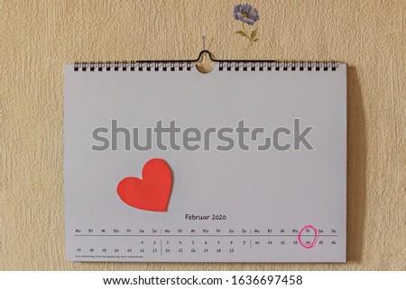 Calendar page with the word "February" in German on a wall with paper hearts and a marked date - February 14th. Valentine's Day.