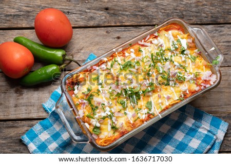 Traditional mexican red baked enchiladas with melted cheese and sour cream on wooden background