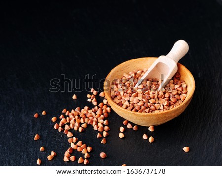 Raw buckwheat grains in wooden bowl with a wooden scoop over black slate (Fagopyrum esculentum)