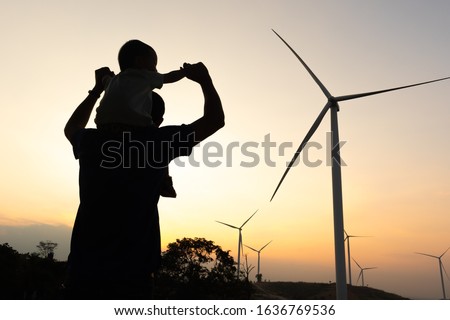 happy father and son playing at the Wind turbines generating electricity. Having quality family time together,Silhouette of wind turbines at sunset. The concept of alternative energy.