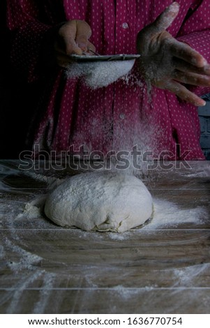 The woman sprinkles flour dough from the fullness for sifting flour, flour falls on the dough, a beautiful scattering of flour. Prepare to make bread and pastries. Front views