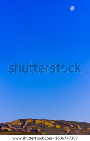 Large blue sky view with mountains and the moon in daylight