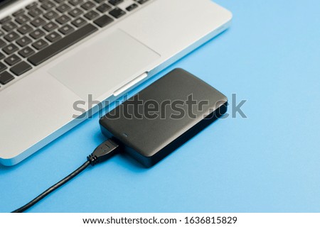External hard disk black , with cable (usb), partial view of laptop, on the blue office table. Top view