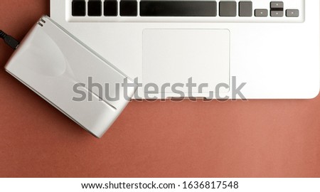 Close-up of aluminum external hard drive on top of laptop, on brown office table.Top view