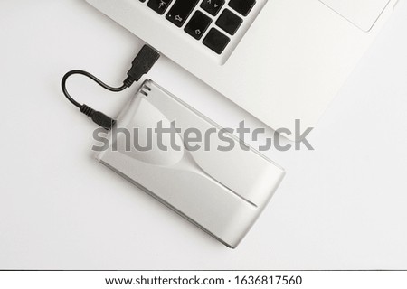 Aluminum external hard drive, with cable (usb) connected to laptop, on the white office table. Top view