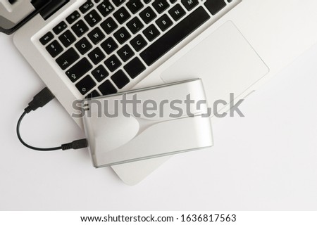 Aluminum external hard drive, with cable (usb) on top of laptop, on the white office table. Top view