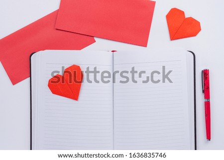The red paper heart shapes and pen on the notebook with envelope over the white background. Greeting cards, Love and Valentines day concept. Flat lay, top view, copy space.
